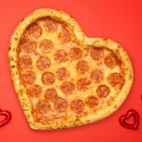 pepperoni pizza berbentuk hati untuk hari kasih sayang dengan latar belakang kertas merah